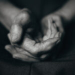 Two old man's hands on a dark background